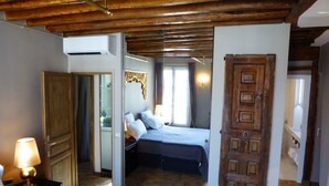 A bedroom with a bed, bedside tables, an air conditioning unit, a wooden door, and a mirror.