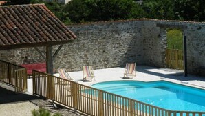Una piscina con cerramiento de madera, rodeada por un muro de piedra y una estructura de techo con tejas.
