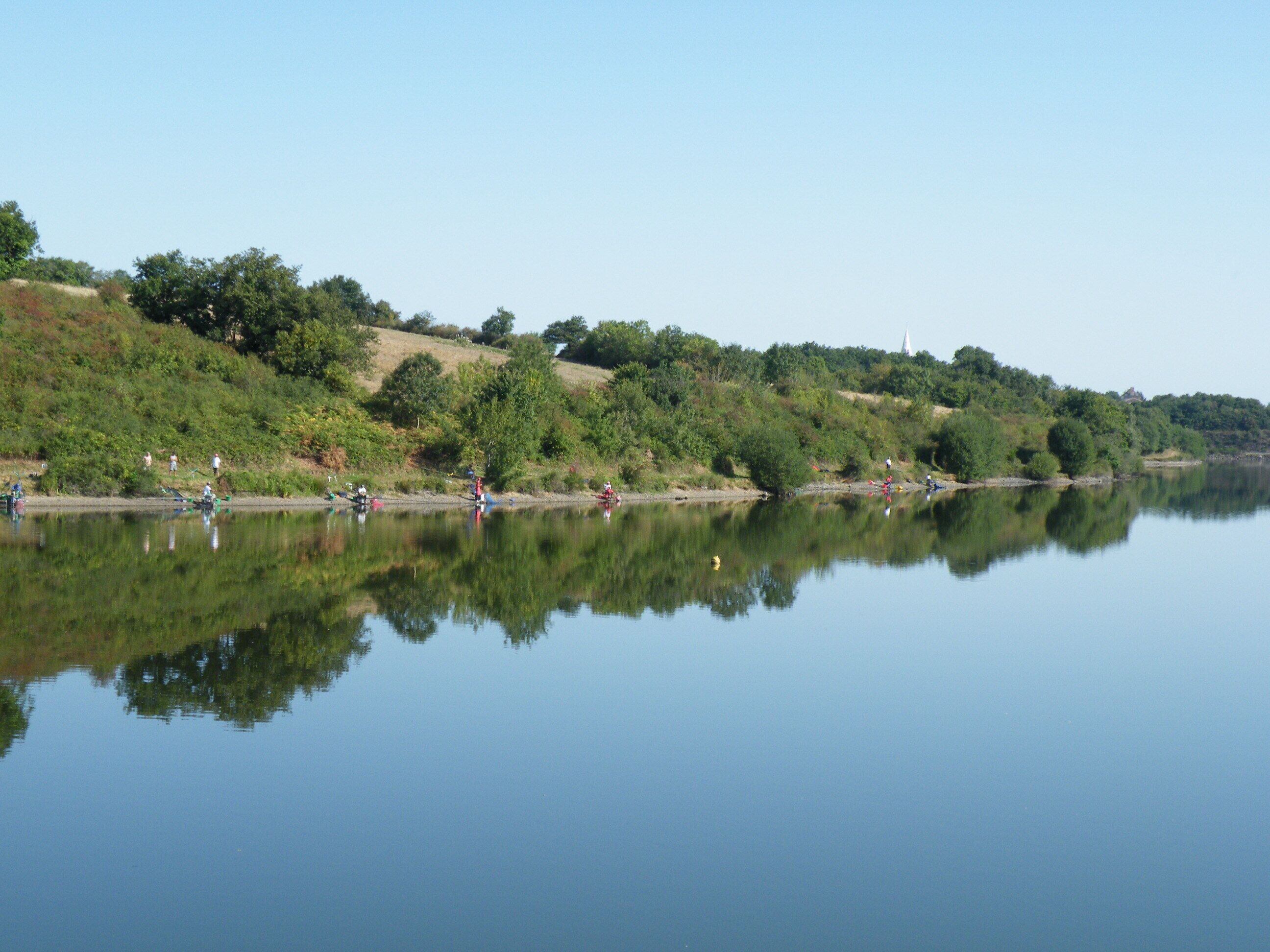 A calm lake with reflections of trees and people.