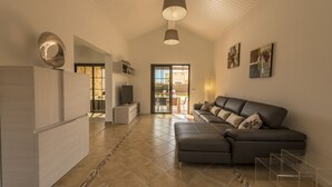 Un salon moderne avec un canapé d’angle, un téléviseur et un coin repas visible à travers une porte vitrée.
