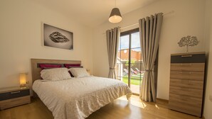 Une chambre à coucher comprenant un lit, une table de chevet, une commode, une fenêtre avec des rideaux et une œuvre d’art accrochée au mur.