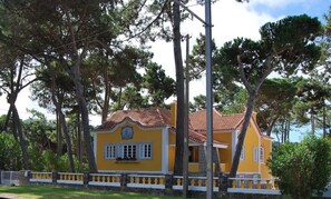 A yellow building with a red-tiled roof, surrounded by trees.