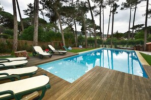 A rectangular swimming pool with a wooden deck and lounge chairs.