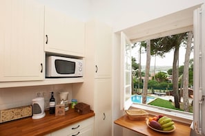 A kitchen with white cabinets, a microwave, and a view of a swimming pool and trees.