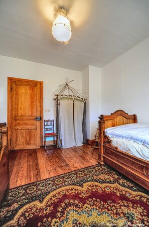 A bedroom with a wooden door, a bed with a headboard, a chair, a hanging plant, and a patterned rug. - Spacious mountain apartment ideal for families (Aubure)