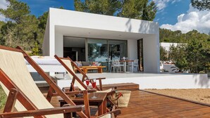 A modern house with a deck, outdoor seating, and a glass door leading to a patio area. - New and modern House with pool in San Jose, 2 people (IBIZA)