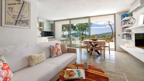 A modern living room with a sofa, coffee table, and a dining area with chairs and a table. There is a large window offering a view of the outdoors. - New and modern House with pool in San Jose, 2 people (IBIZA)