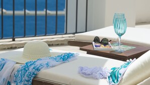 A sun lounger with a hat, a glass, and sunglasses on a wooden table, overlooking the sea.