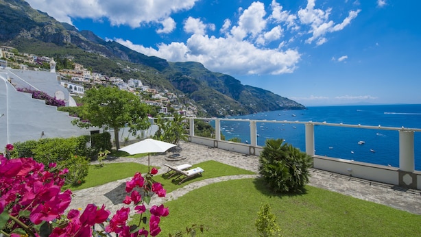 A coastal property with a patio, a view of the sea, and a mountainous backdrop.