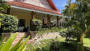 A traditional house with a red roof, a covered porch, and a well-maintained garden with various plants and a small pond.