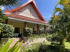 A traditional house with a red roof, a covered porch, and a well-maintained garden with various plants and a small pond.