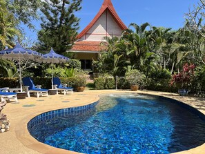 Une piscine aux carreaux bleus, entourée de chaises longues et de parasols, avec un bâtiment en arrière-plan.