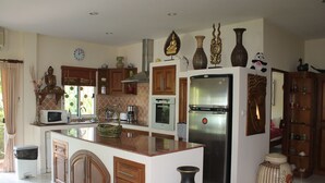 A kitchen with a central island, wooden cabinets, a stainless steel refrigerator, and decorative items on the walls.