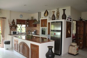A kitchen with a central island, wooden cabinets, a stainless steel refrigerator, and decorative items on the walls.