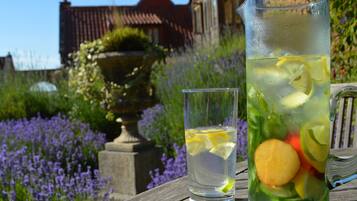 En kande og et glas fyldt med vand og citronskiver på et træbord med udsigt til en have.