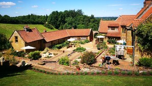 A traditional stone building with a tiled roof, surrounded by a well-maintained garden with various plants and a barbecue area. - The cosiest and quaintest haven for couples, near Great Tew (Chipping Norton)