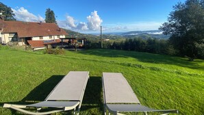 Une maison avec un toit recouvert de tuiles rouges, une cour gazonnée et deux tables de pique-nique en métal.