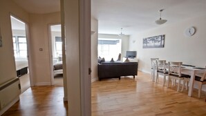 An open-plan living area with a sofa, dining table, and chairs. A television is mounted on the wall. - Toothbrush Apartments - Central Ipswich - St Peters St (Ipswich)