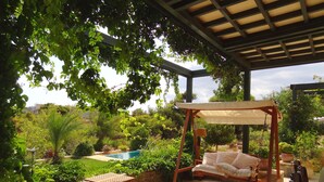 A covered patio with a swing chair, a small table, and a view of a swimming pool.