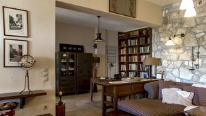 A cozy living room with a wooden sofa, a coffee table, and a bookshelf filled with books. There is a clock on the wall and a lamp on the table.