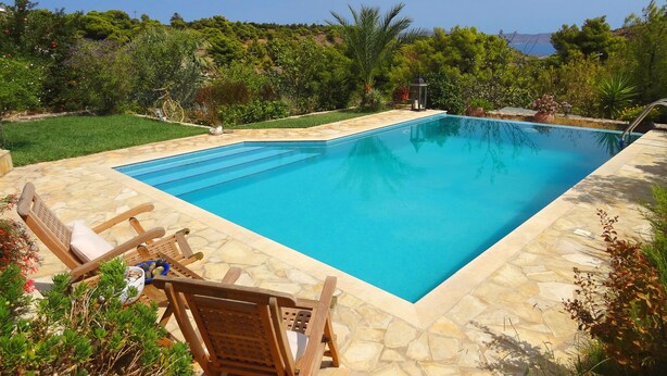 A rectangular swimming pool with stone tiles, surrounded by a well-maintained lawn and various plants.