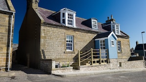 Un bâtiment en pierre avec un toit en pente, un escalier en bois et un petit porche doté d’une balustrade.