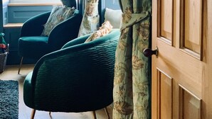 Une pièce avec une grande porte en bois, une fenêtre avec des rideaux, un fauteuil vert et un lit avec un oreiller.