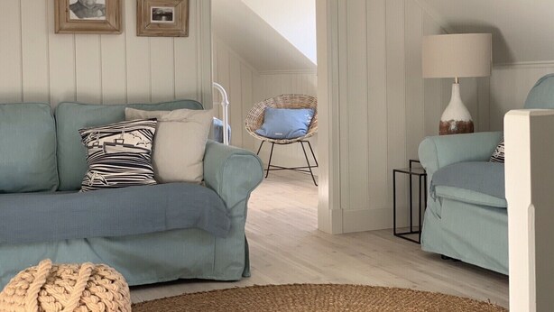 Un salon chaleureux avec un plafond haut, un canapé bleu, un fauteuil en osier et une lampe.
