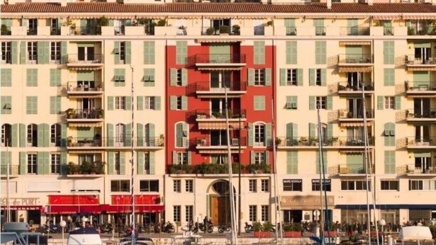 A multi-story building with balconies, a central red section, and a marina with boats in front. - Chic studio with terrace and beautiful view of the port, 100m from the beach, parking available (Nice)
