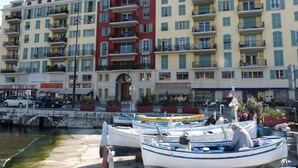 A waterfront building with multiple balconies, a café, and boats docked in front. - Chic studio with terrace and beautiful view of the port, 100m from the beach, parking available (Nice)