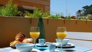 A table set with croissants, orange juice, and coffee cups, overlooking a scenic view with greenery and a building in the background. - Chic studio with terrace and beautiful view of the port, 100m from the beach, parking available (Nice)