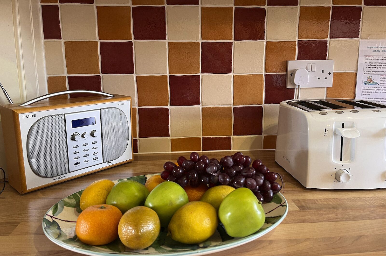 Una encimera de cocina con una radio, un tostador y un plato de frutas.