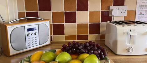 Una encimera de cocina con una radio, un tostador y un plato de frutas.