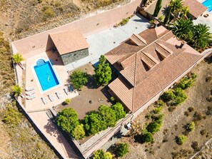 Ovenudblik over et resort med en swimmingpool, liggestole og et anlagt område med træer.