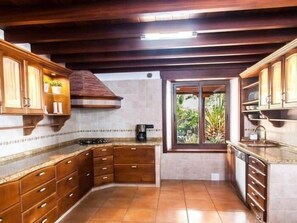 A kitchen with wooden cabinets, a gas stove, and a window with a view of greenery. - Beautiful Holiday Home With Pool (Adeje)