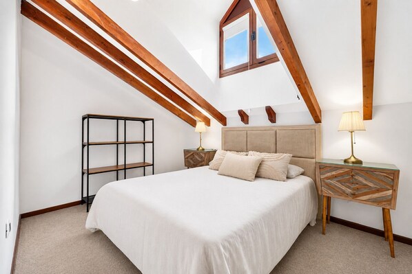 A bedroom with a bed, wooden beams, a window, a bedside table with a lamp, and a bookshelf. - Beautiful Holiday Home With Pool (Adeje)