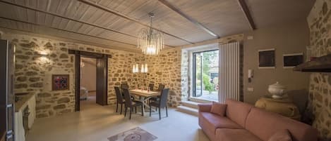 A spacious living area with a stone wall, a dining table with chairs, a pink sofa, and a chandelier.