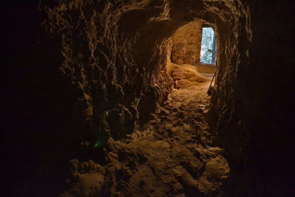 A narrow, dimly lit passageway with rough stone walls and a small window at the end.