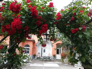 Une cour avec une pergola recouverte de roses rouges, une porte blanche et une table entourée de chaises.