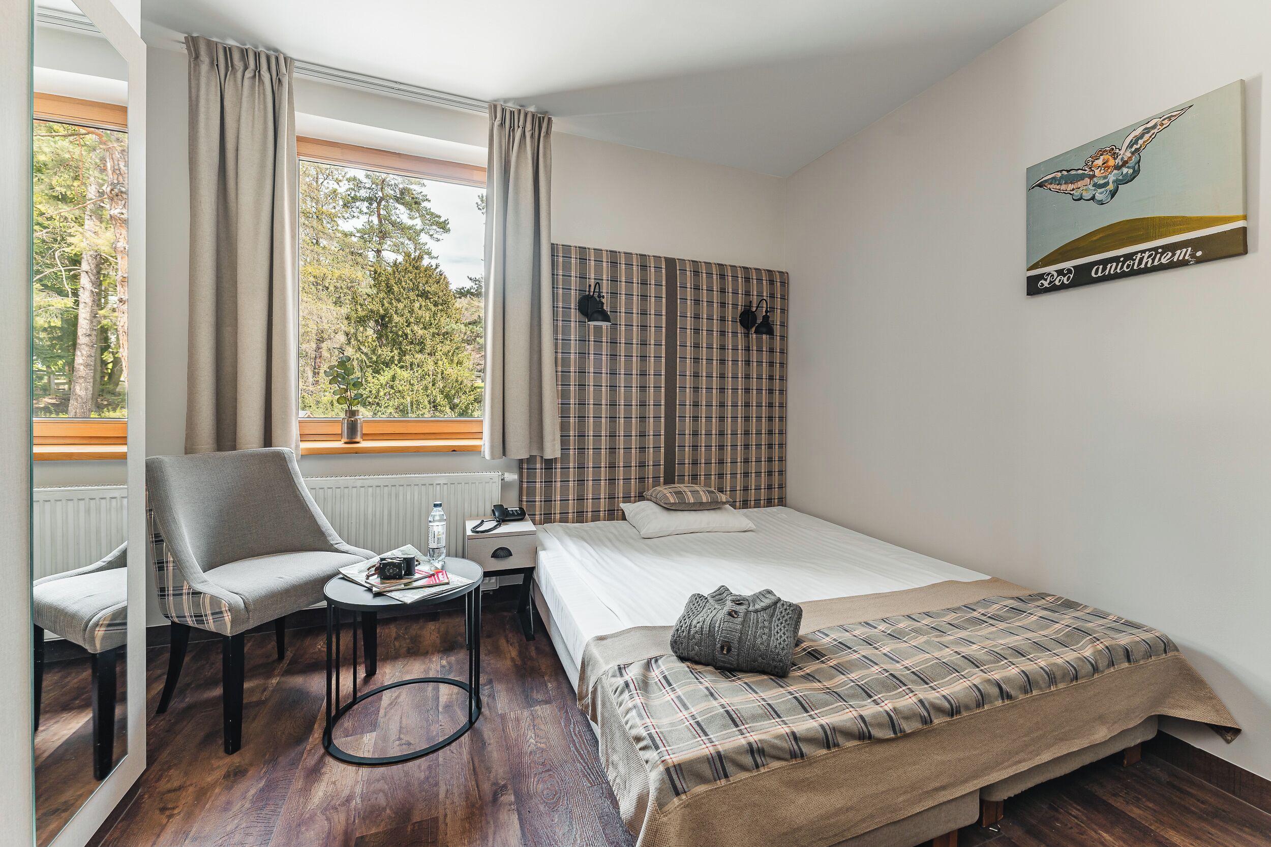 A hotel room with a bed, a chair, a small table, and a window with curtains.