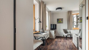 Habitación pequeña y bien iluminada con suelo de madera, escritorio con lámpara, silla, televisor y radiador.