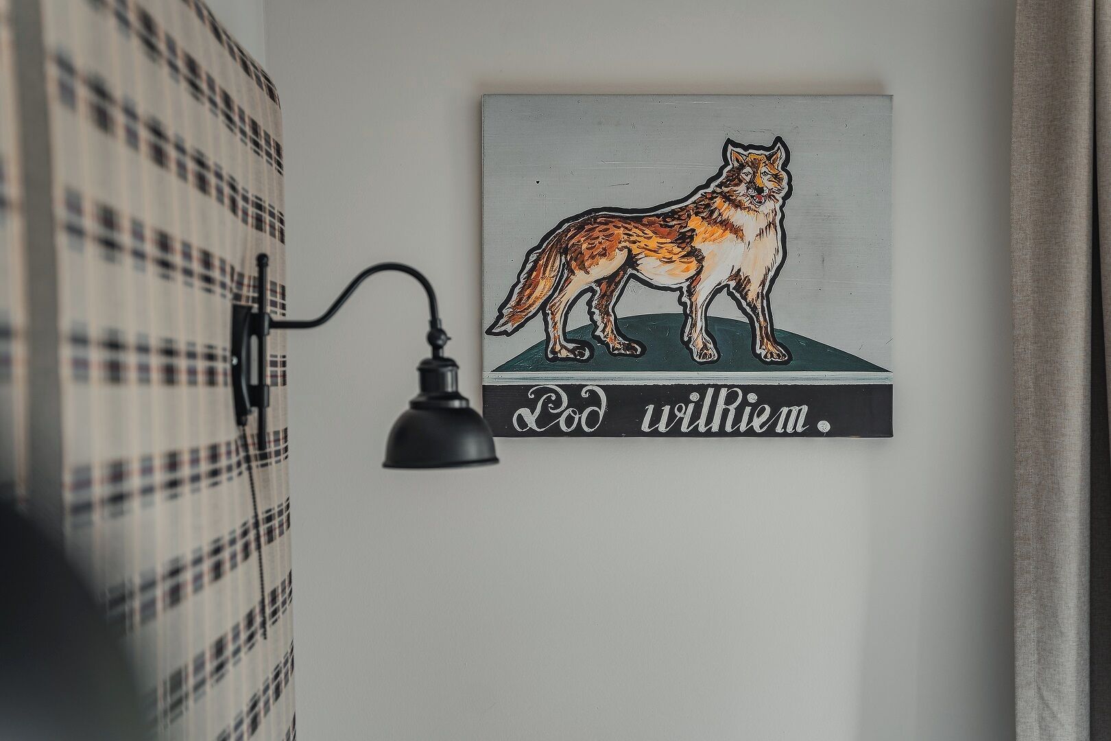 A wall-mounted lamp and a framed artwork of a wolf with the text "Pod wilRiem."