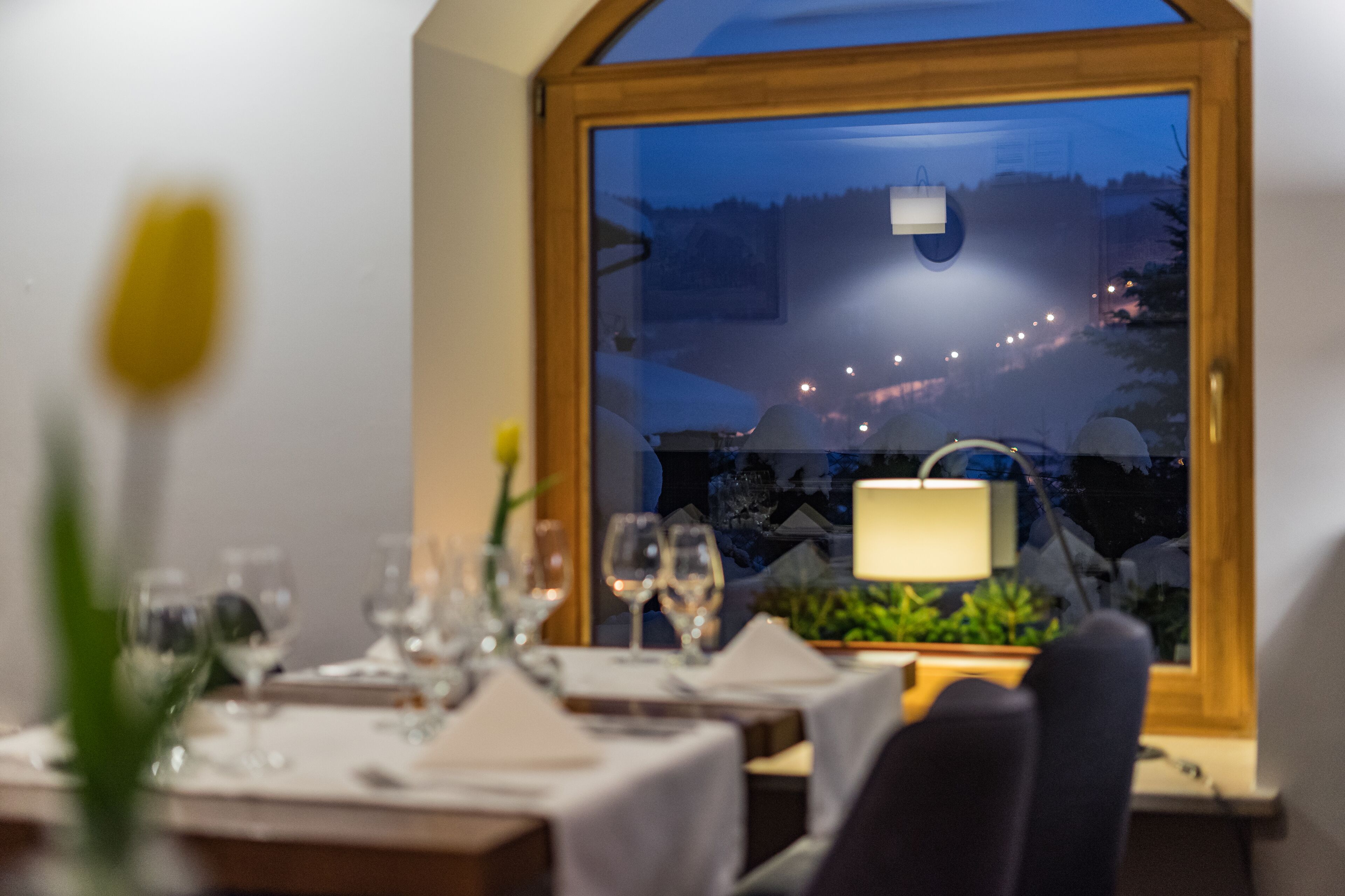A dining table set with glasses and a vase, a window with a view of a snowy landscape, and a lamp on the table.