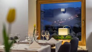 A dining table set with glasses and a vase, a window with a view of a snowy landscape, and a lamp on the table.