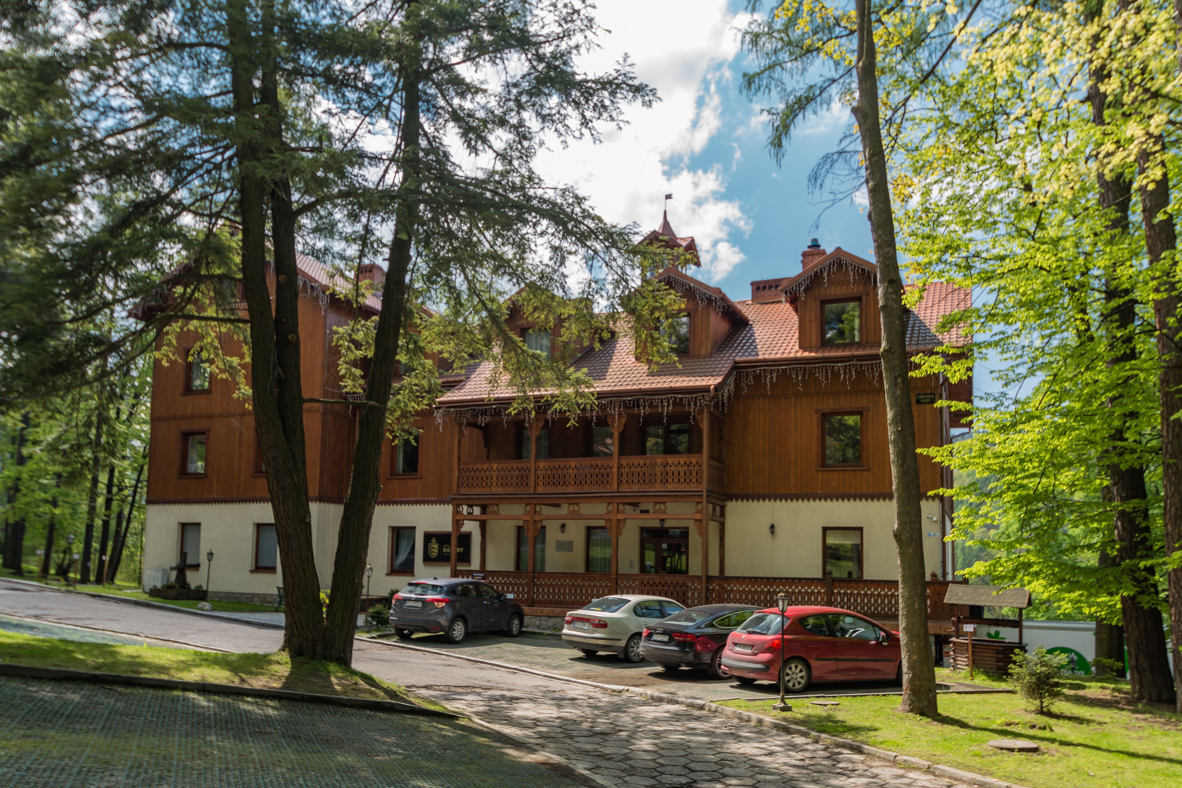En traditionell byggnad i trä med en balkong, parkerade bilar och träd.