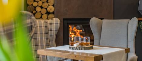 Un rincón acogedor con una chimenea, cojines de cuadros y una mesa con vasos de whisky.