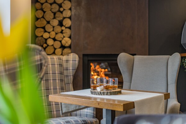 A cozy seating area with a fireplace, plaid cushions, and a table with glasses of whiskey. - Hotel Batory (Szczawnica)
