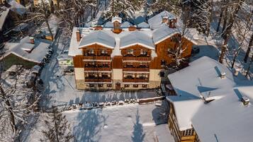 Un edificio de madera grande y de varios pisos con balcones, rodeado de árboles cubiertos de nieve y un cielo despejado.