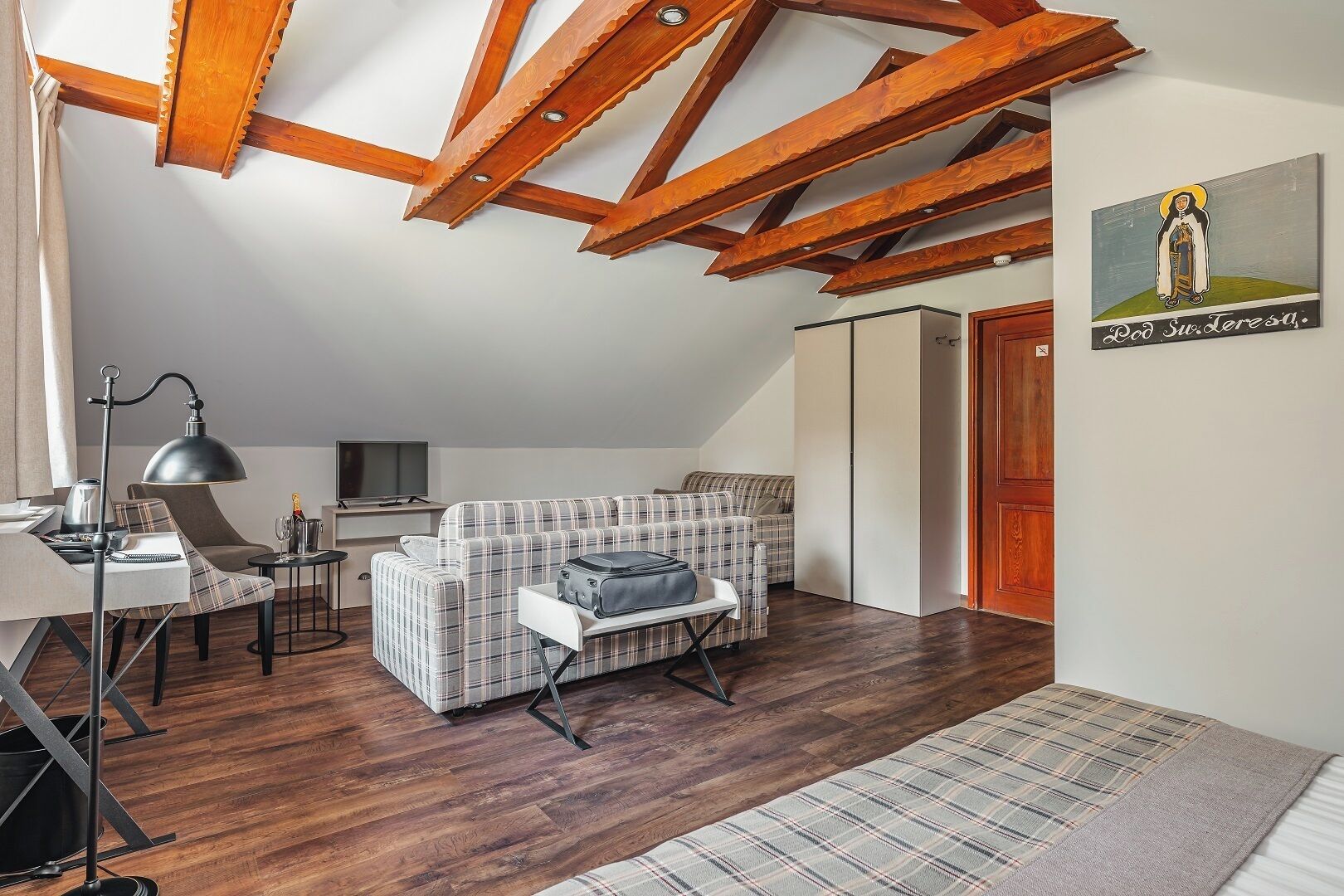 Une pièce confortable de style loft, avec un plafond haut, des poutres en bois, un canapé à carreaux, une petite table à manger et un téléviseur.