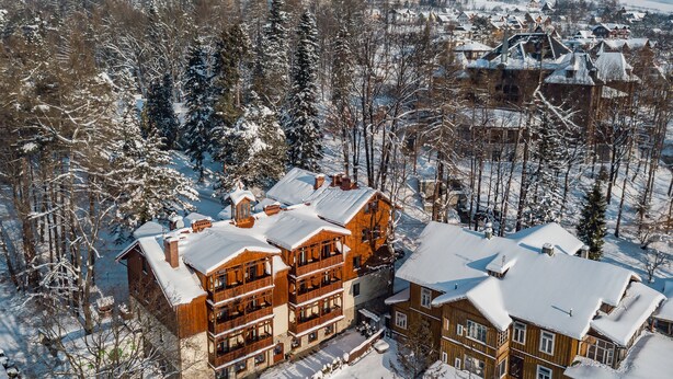 Un edificio de madera de varios pisos con balcones, rodeado de árboles nevados y un cielo despejado.